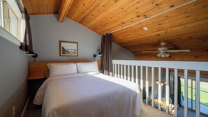 Une chambre avec un plafond en bois, un lit avec une literie blanche, un tableau au mur et un balcon agrémenté de mobilier d’extérieur.