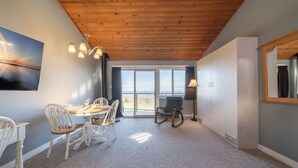 Une pièce avec un plafond en bois, une table à manger avec des chaises, un fauteuil à bascule et une grande fenêtre donnant sur un beau paysage.