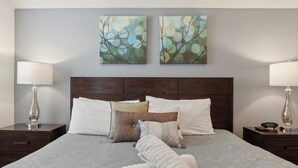 Un lit bien fait, recouvert d’une couvre-lit à motifs, deux tableaux accrochés au mur et deux lampes de chevet.