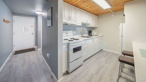 A modern kitchen with white cabinets, a built-in oven, and a bar area with stools. - #222 Upper Beach View Suite at Shorewater Resort, Qualicum Beach (Qualicum Beach)