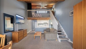 A cozy living room with a wooden ceiling, a staircase, a sofa, a coffee table, and a TV. - #222 Upper Beach View Suite at Shorewater Resort, Qualicum Beach (Qualicum Beach)