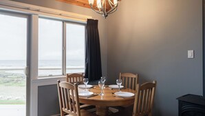 A dining area with a round wooden table, four chairs, and a view of the sea through large windows. - #222 Upper Beach View Suite at Shorewater Resort, Qualicum Beach (Qualicum Beach)