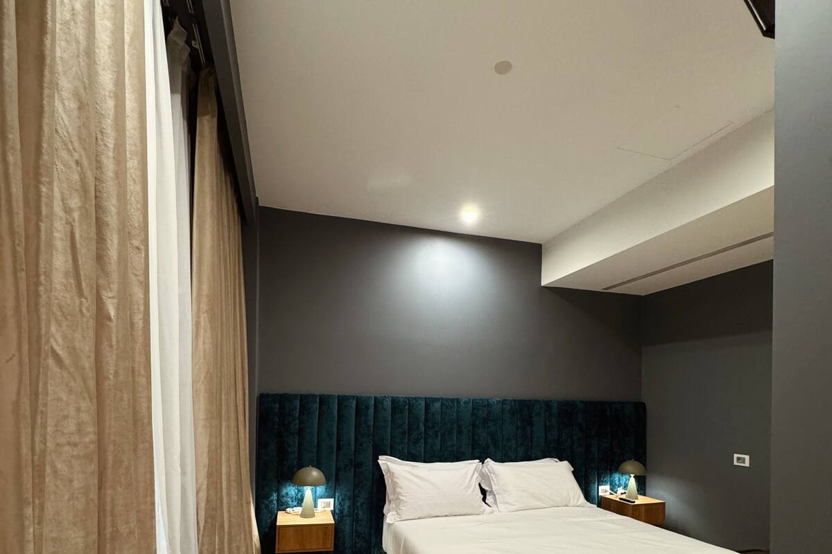Un dormitorio moderno con una cama grande, dos mesitas de noche, un cabecero y una silla color turquesa.