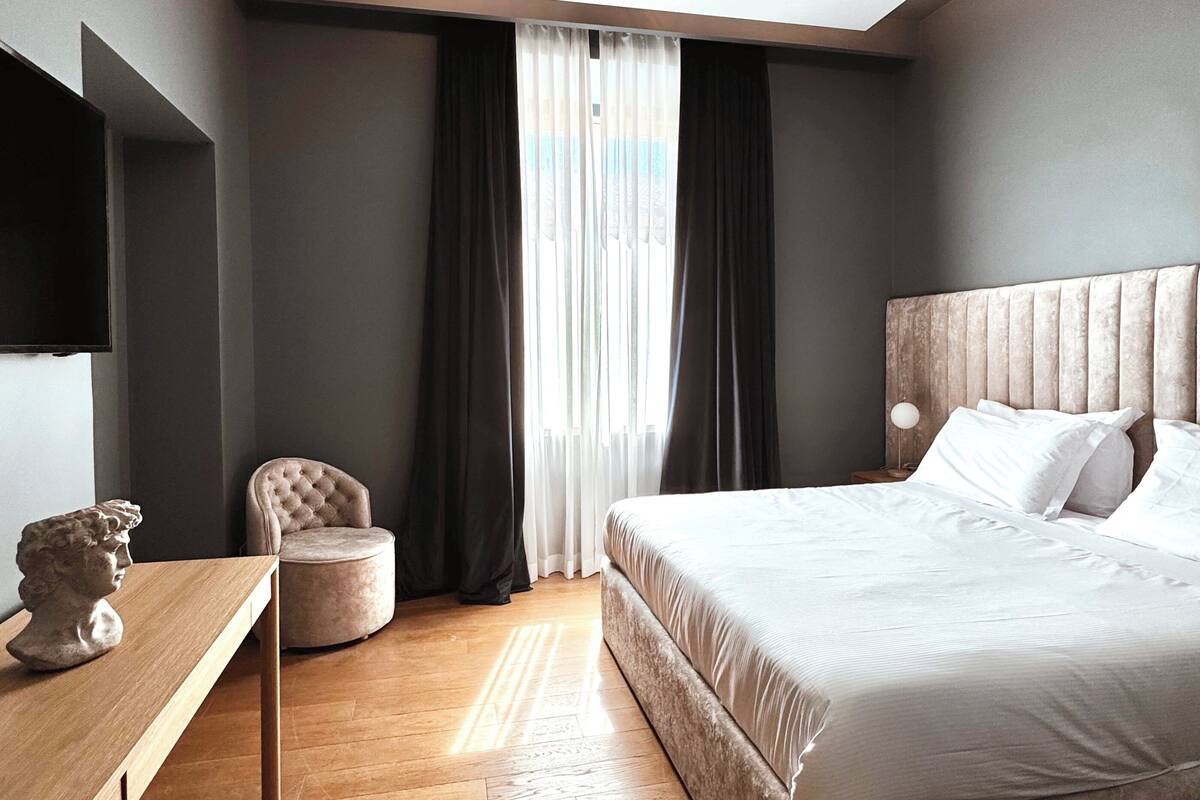 Un dormitorio moderno con una cama grande, un escritorio de madera, una silla y un televisor en la pared.