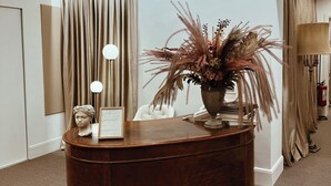 En receptionsdisk med en vase med tørrede planter, en brystbillede skulptur og et indramet dokument.