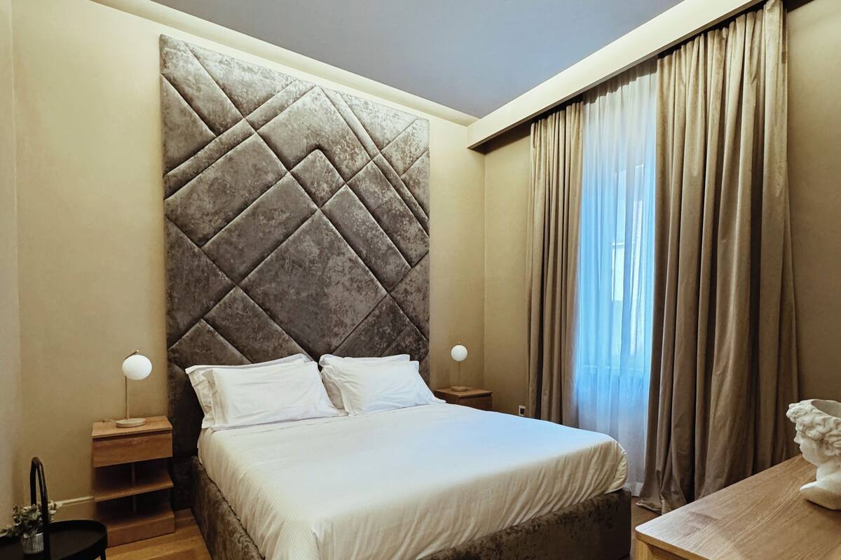 Un dormitorio con una cama grande, una mesita de noche de madera, una pequeña mesa y una silla.