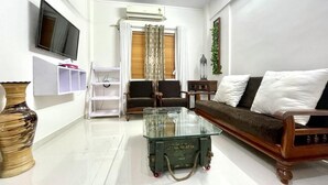Un salon avec une table basse en verre, un canapé, un téléviseur et un ventilateur de plafond.