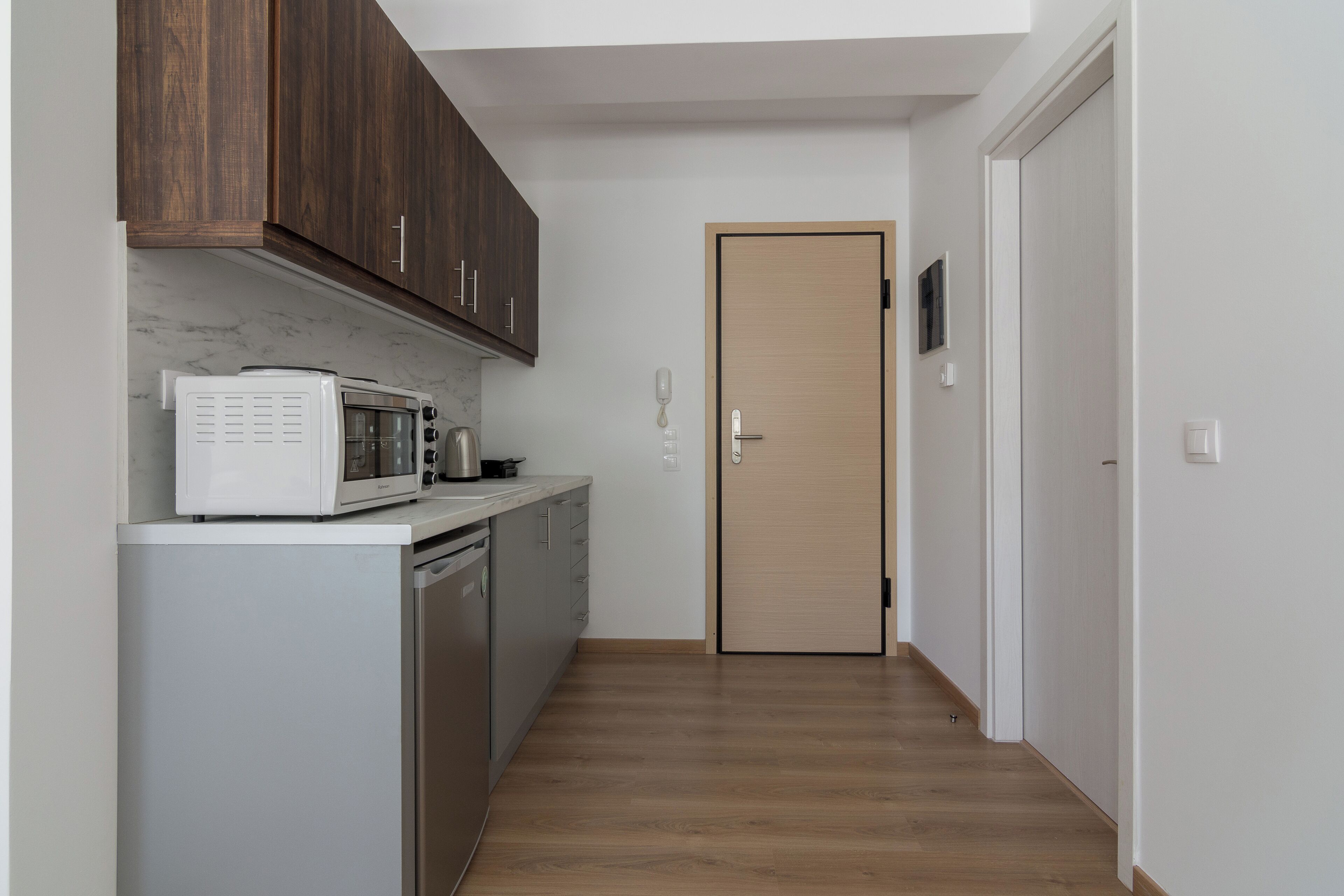 Une cuisine compacte équipée d’un four à micro-ondes, d’un grille-pain et d’un lave-vaisselle. Une porte en bois donne sur un couloir.