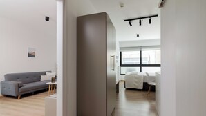 Una sala moderna con un sofá gris, una mesita pequeña y un centro de mesa blanco. Hay un mueble gris grande y una ventana con vistas a la ciudad.
