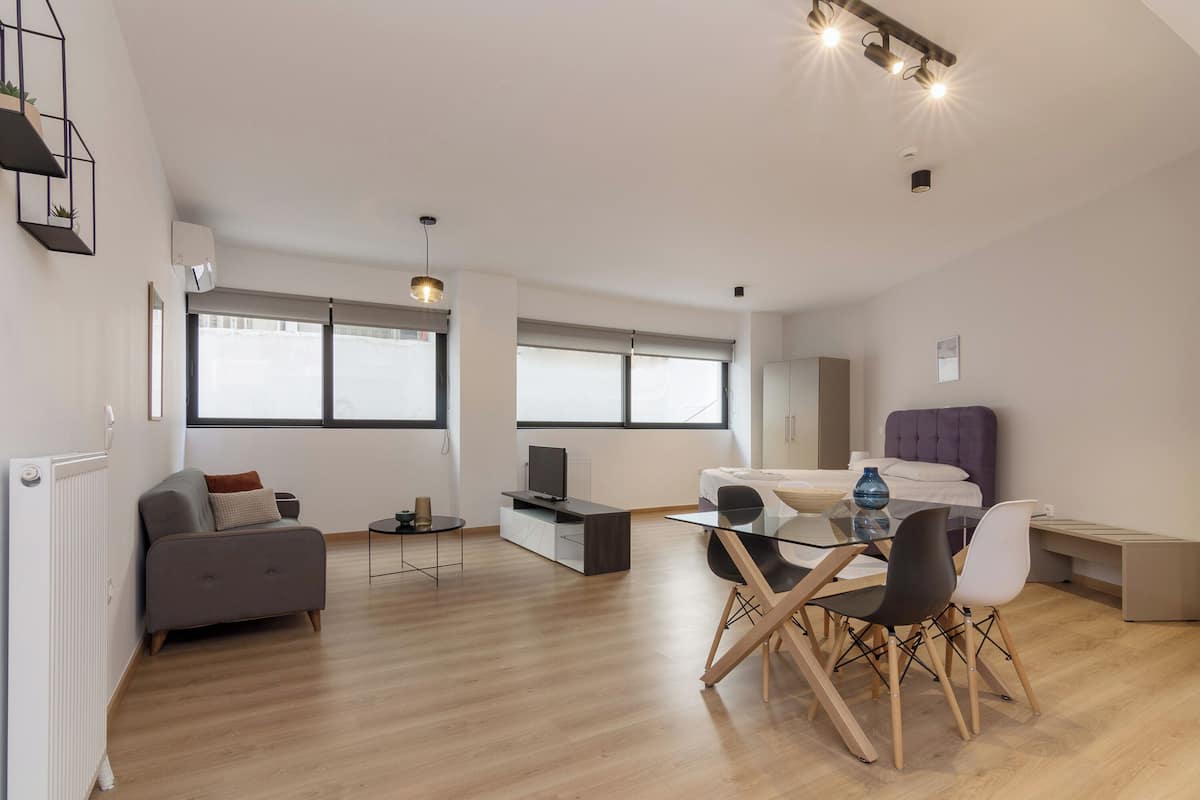 Een moderne woonkamer met een bank, een glazen eettafel met stoelen, een televisie en een groot raam.