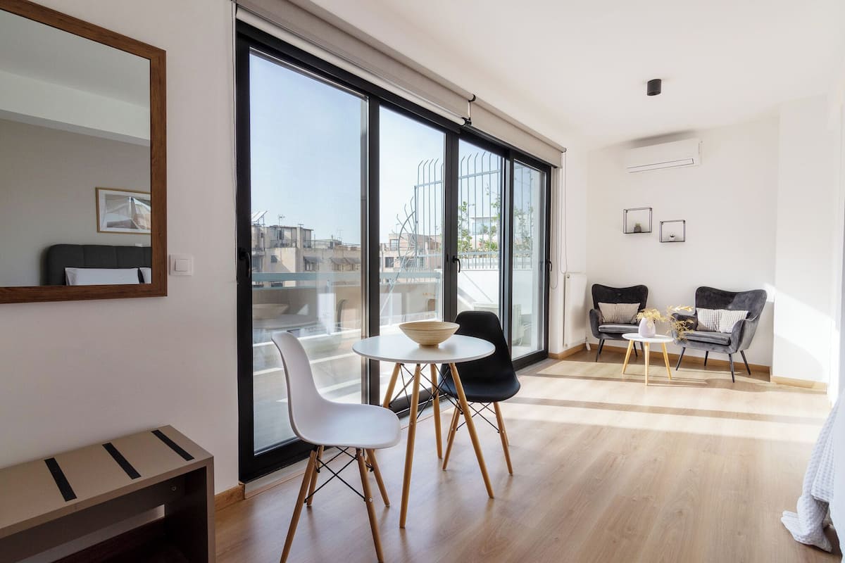Een moderne woonkamer met een grote schuifpui die leidt naar een balkon, een ronde tafel met stoelen, en twee banken.