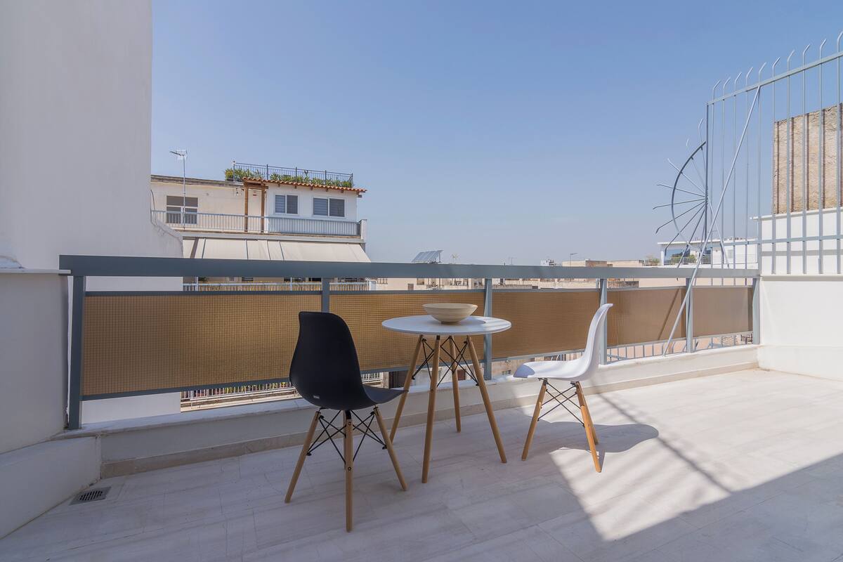 Een terras op het dak met een tafel, stoelen en een uitzicht op gebouwen, met een metalen hekwerk.