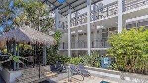 A hotel with a pool area, lounge chairs, and a thatched-roof structure.