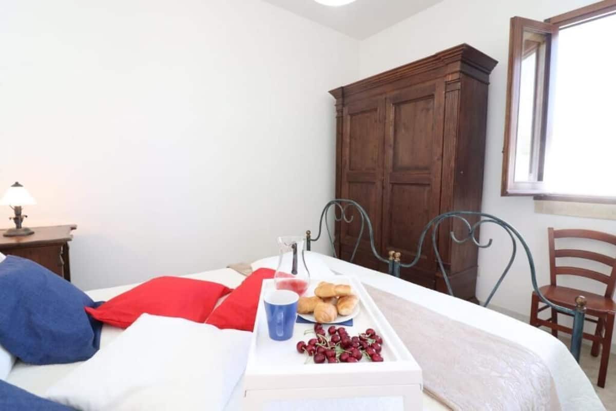 Une chambre à coucher avec un lit, une table de chevet avec une lampe, une armoire en bois et une fenêtre.