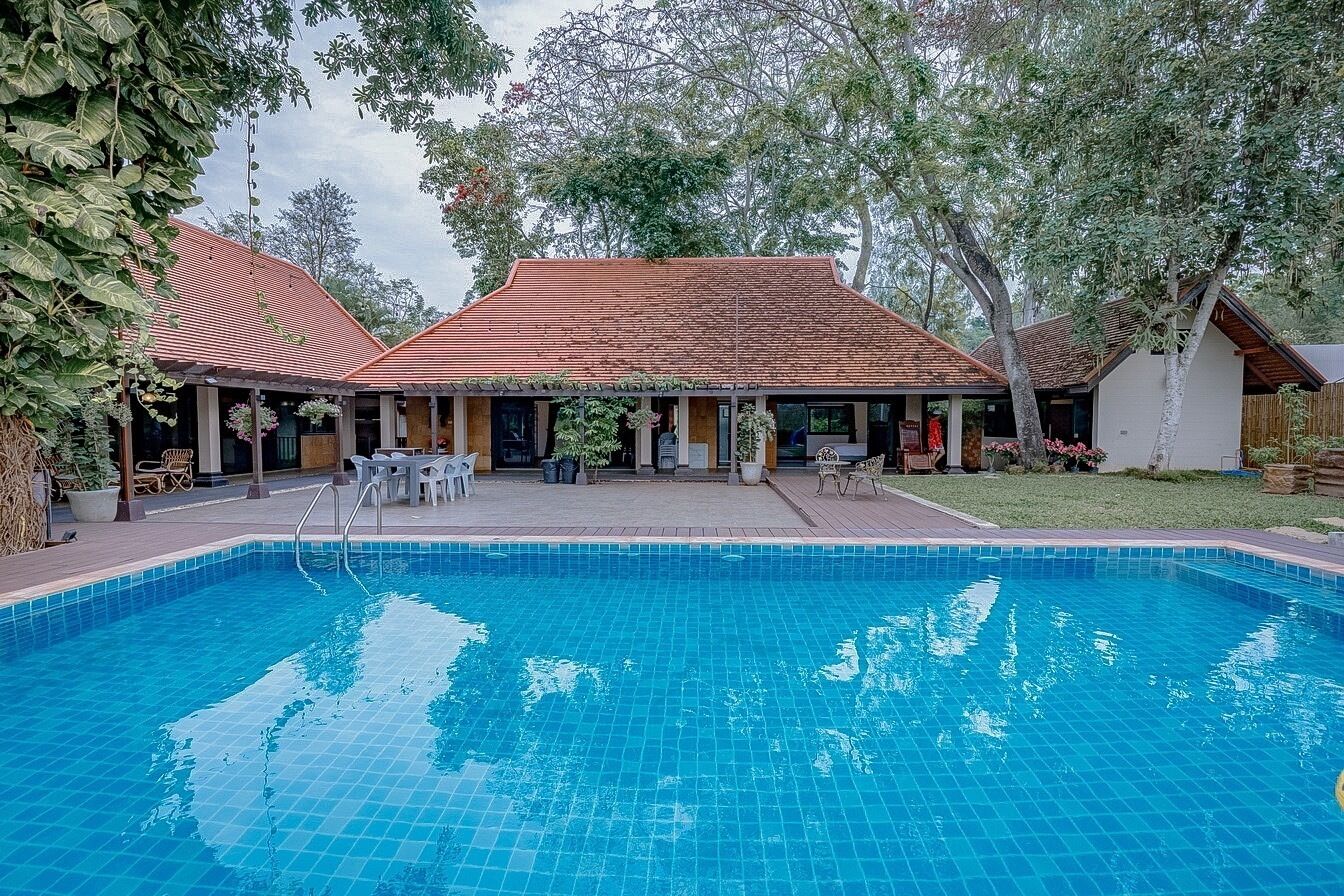 Una piscina con cubierta de baldosas, rodeada por un porche techado con mobiliario de exterior.