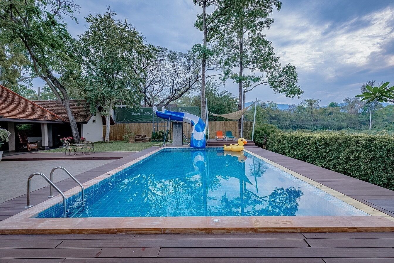 Ein Schwimmbecken mit Rutsche, umgeben von Bäumen und Blick auf ferne Hügel.