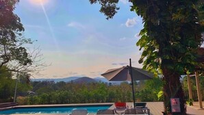 An outdoor pool area with a table and chairs, surrounded by lush greenery and mountains in the background. - Khaoyai Valley 4 (Pak Chong)