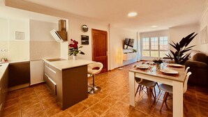 Una cocina moderna con una isla central, un área de comedor con una mesa preparada para dos personas, y un ventanal que proporciona luz natural.