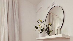 Un baño con una silla negra, un estante blanco con un espejo y una planta en maceta.