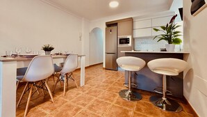 Cocina compacta con zona de comedor, que incluye un refrigerador moderno, un horno empotrado y un pequeño bar con taburetes.