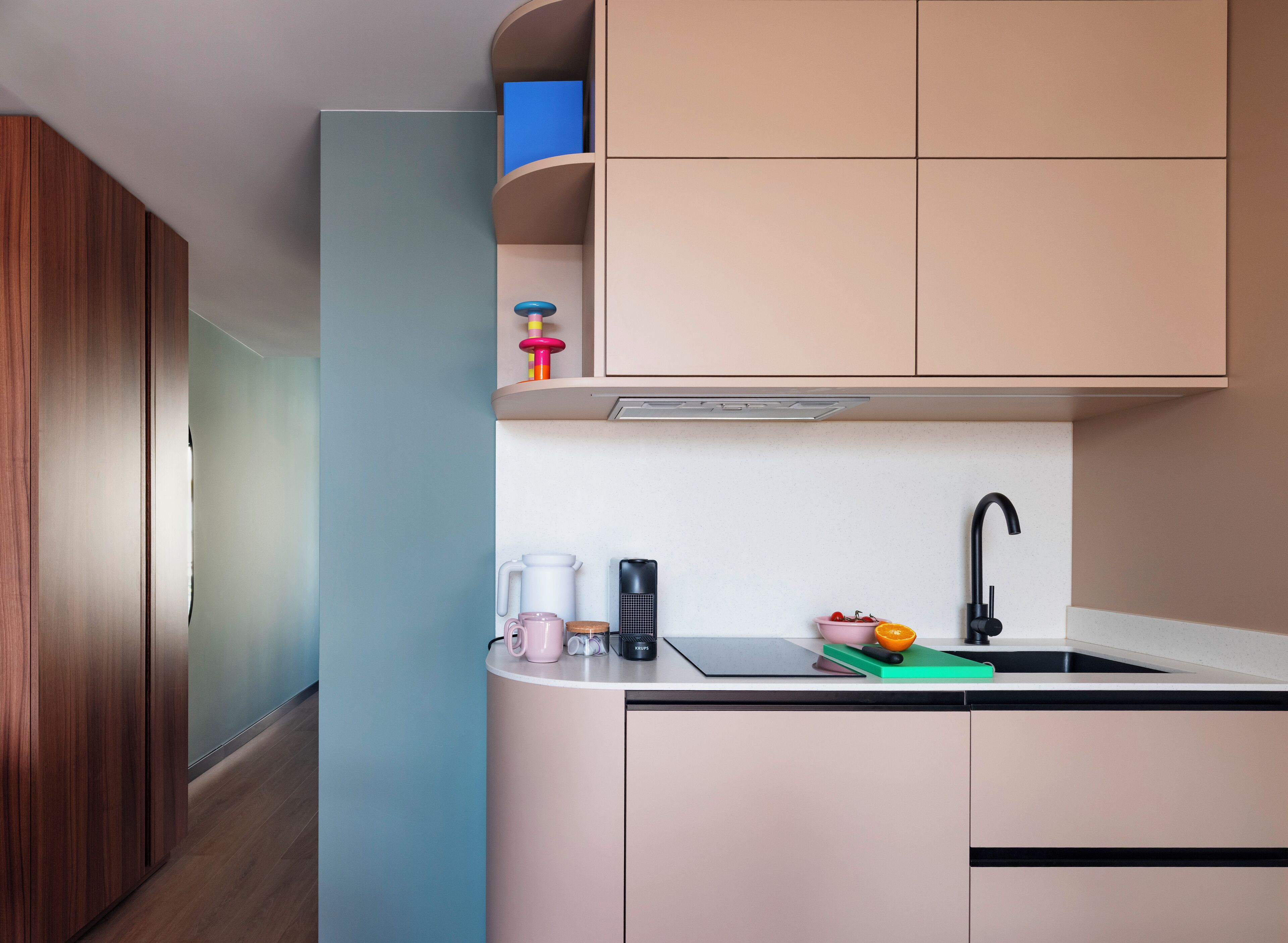 A modern kitchen with a built-in oven, a sink with a black faucet, and a countertop with a coffee maker, mug, and fruit bowl.