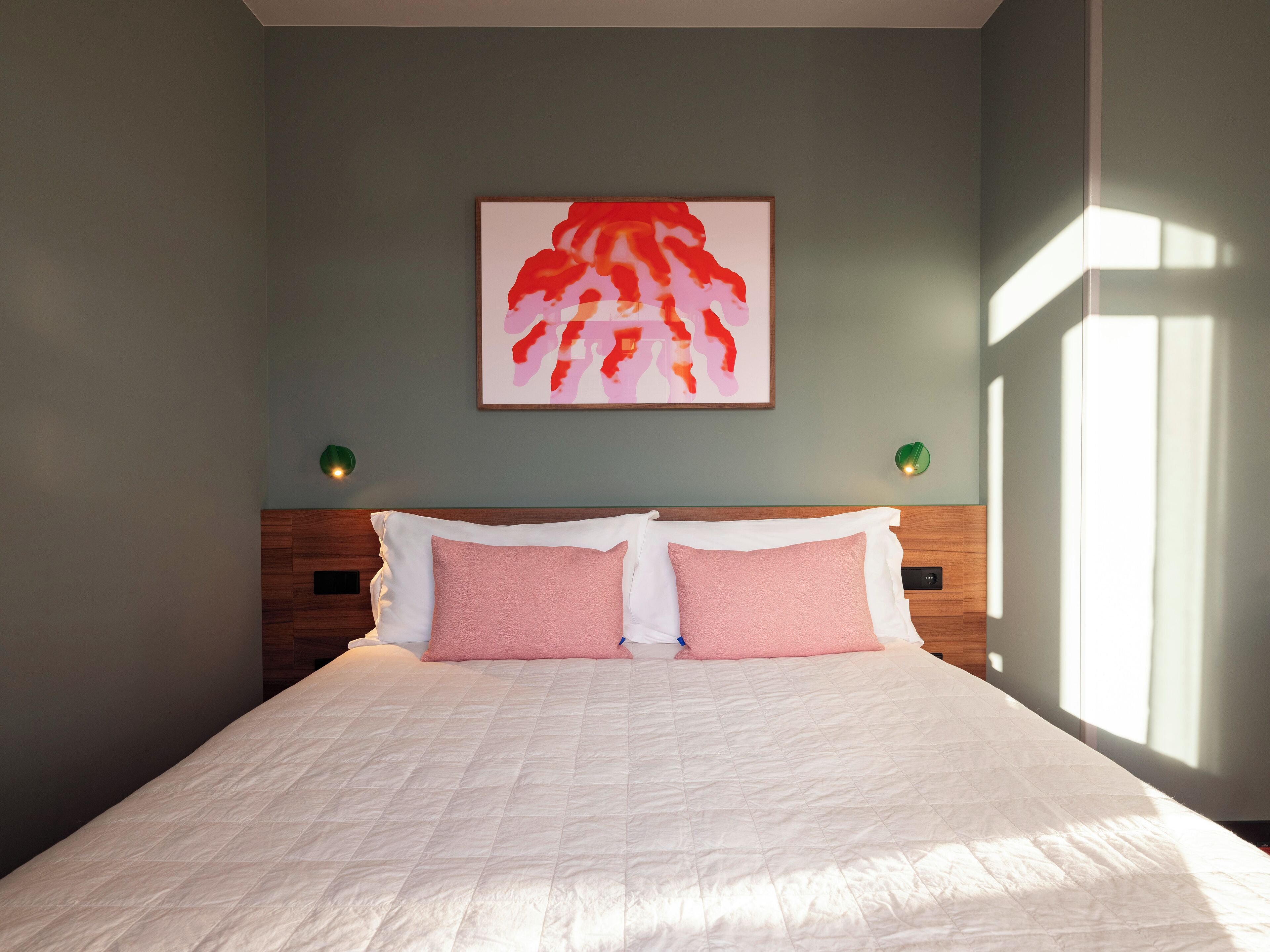 A bedroom with a large bed, a headboard, a wall-mounted painting, and two bedside lamps.