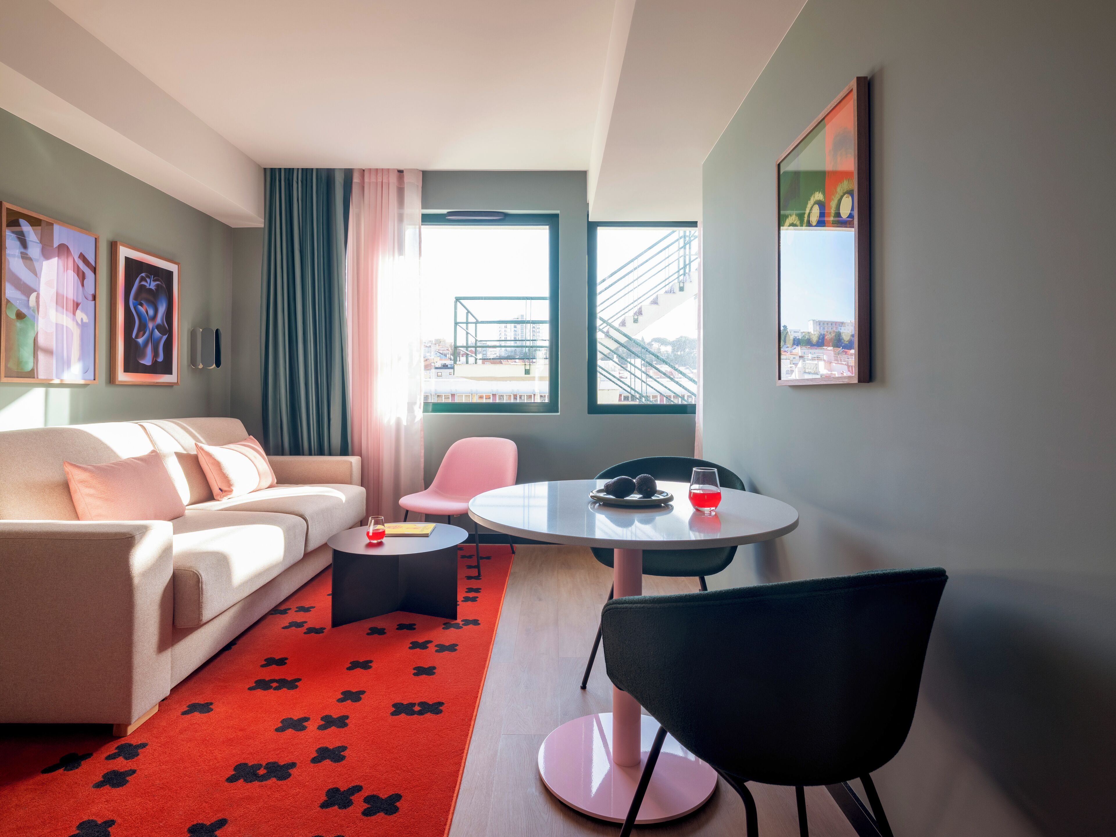 A modern living room with a sofa, a pink chair, a round table with a glass of red drink, and a red carpet with black floral patterns.
