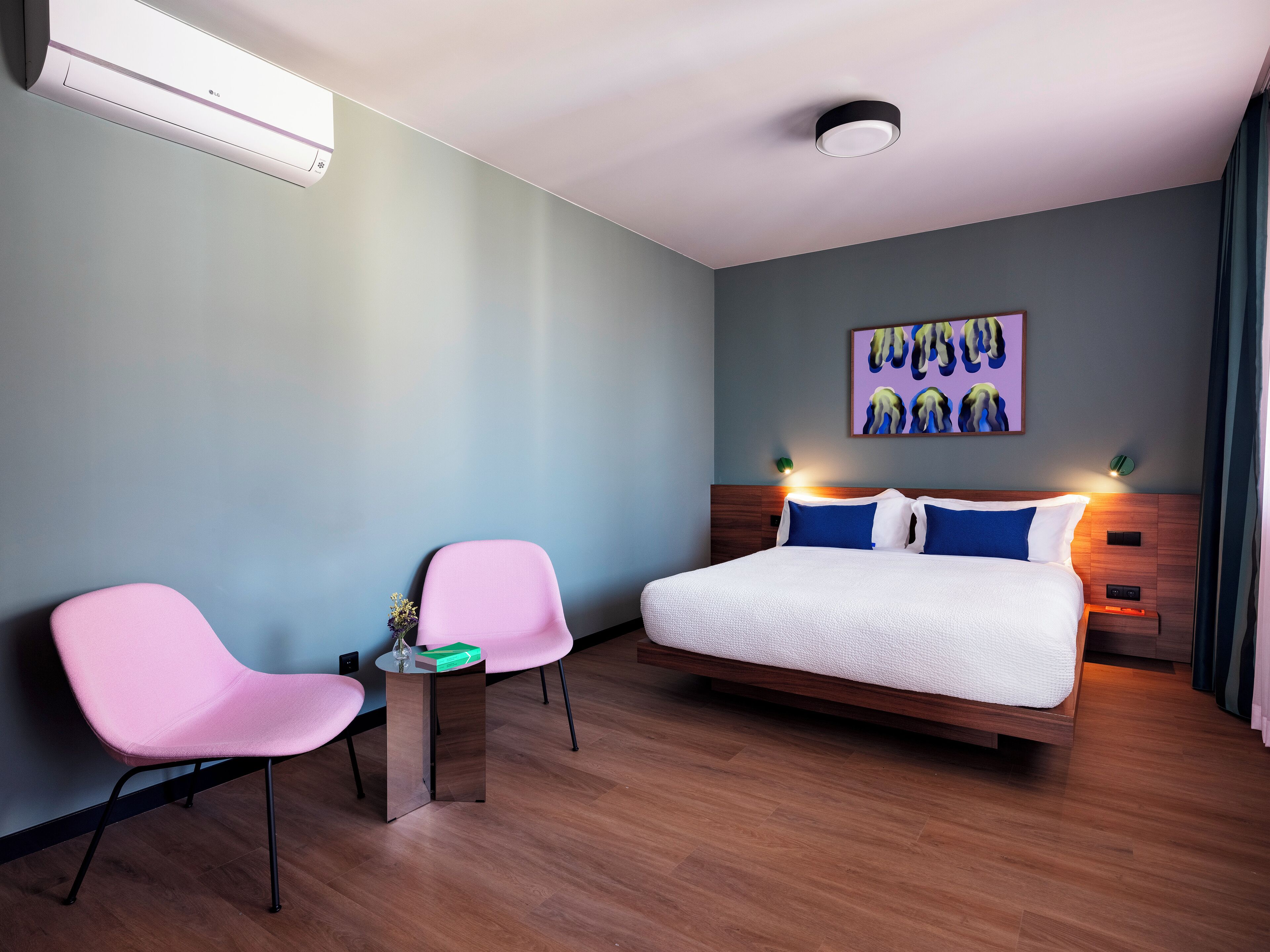 Ein modernes Hotelzimmer mit einem großen Bett, zwei rosa Stühlen, einem kleinen Tisch und einem Bild an der Wand.