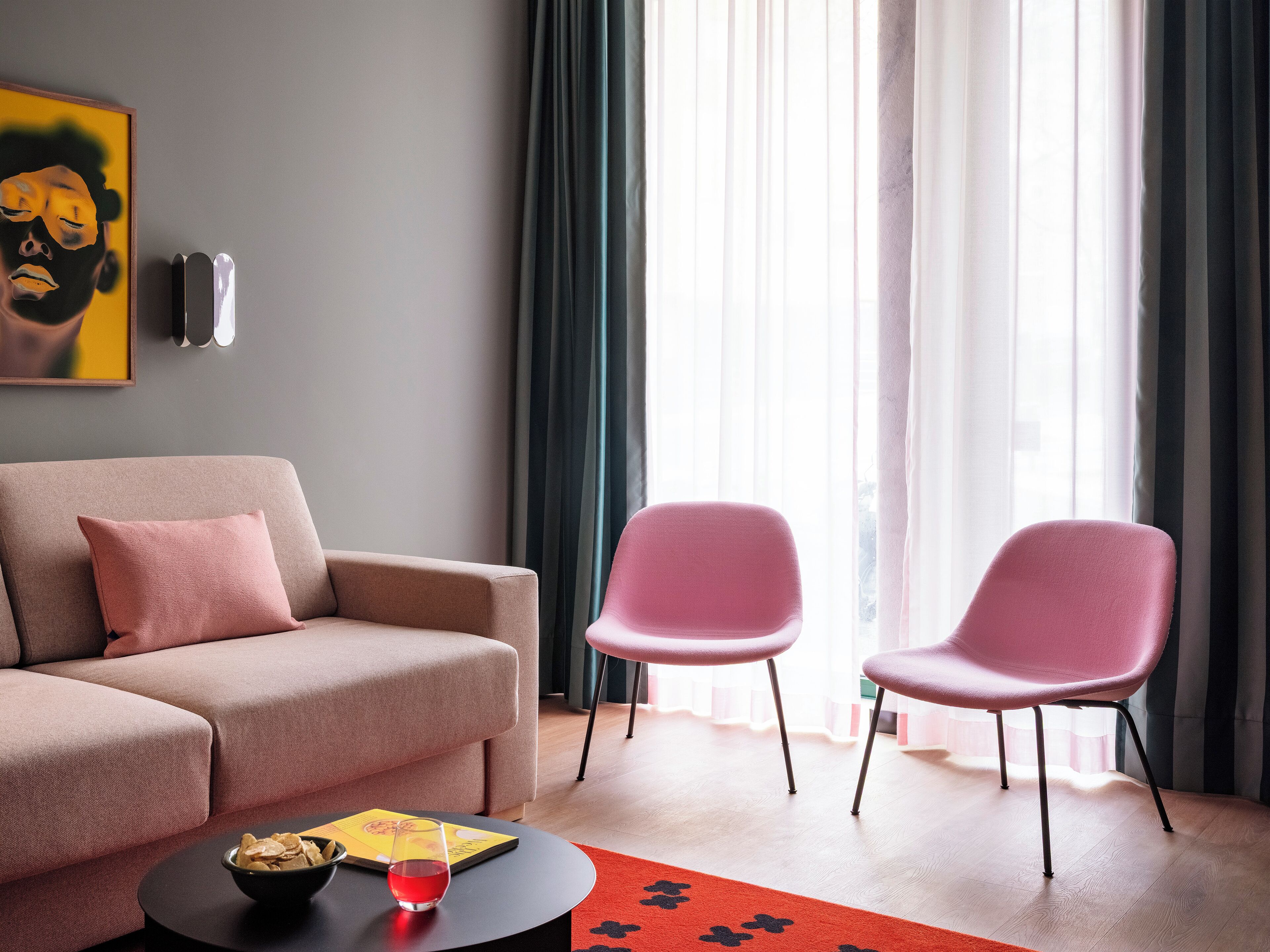A modern living room with a sofa, two chairs, a coffee table with a glass and a book, and a painting on the wall.