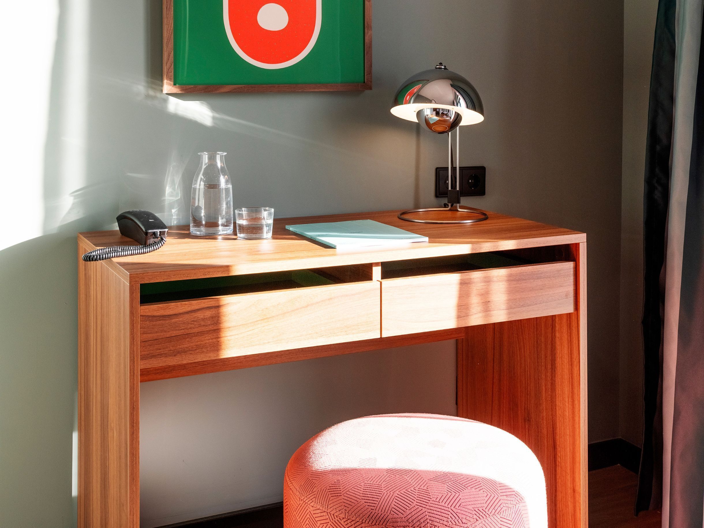 Una scrivania in legno con una lampada, un telefono, due bottiglie e un bicchiere.