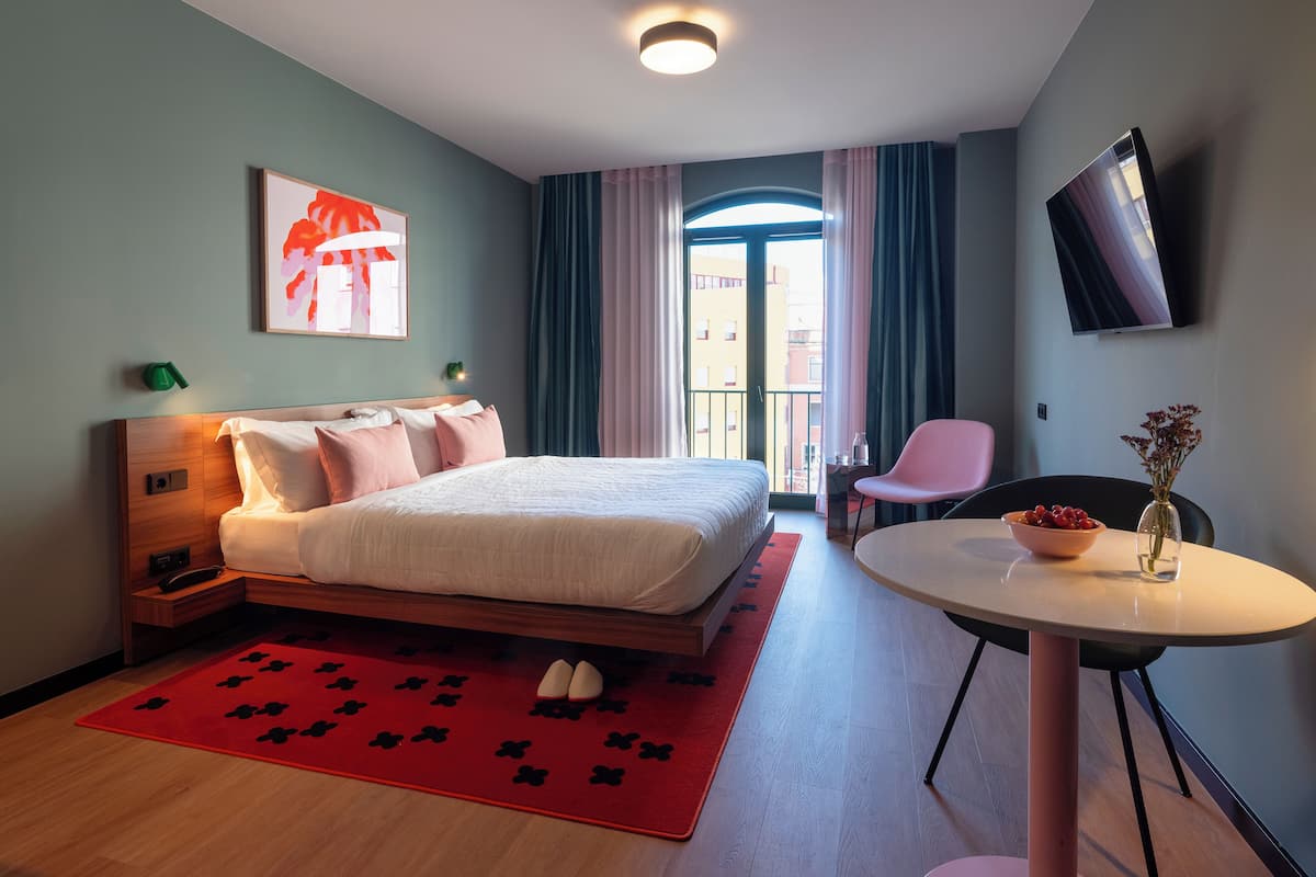 Een hotelkamer met een bed, een bureau, een stoel, een televisie en een raam met gordijnen.