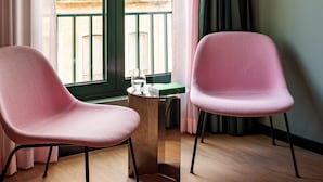 Two pink chairs, a wooden table with a glass and a book, and a window with a view of buildings. - Numa Lisbon Anjos (Lisbon)