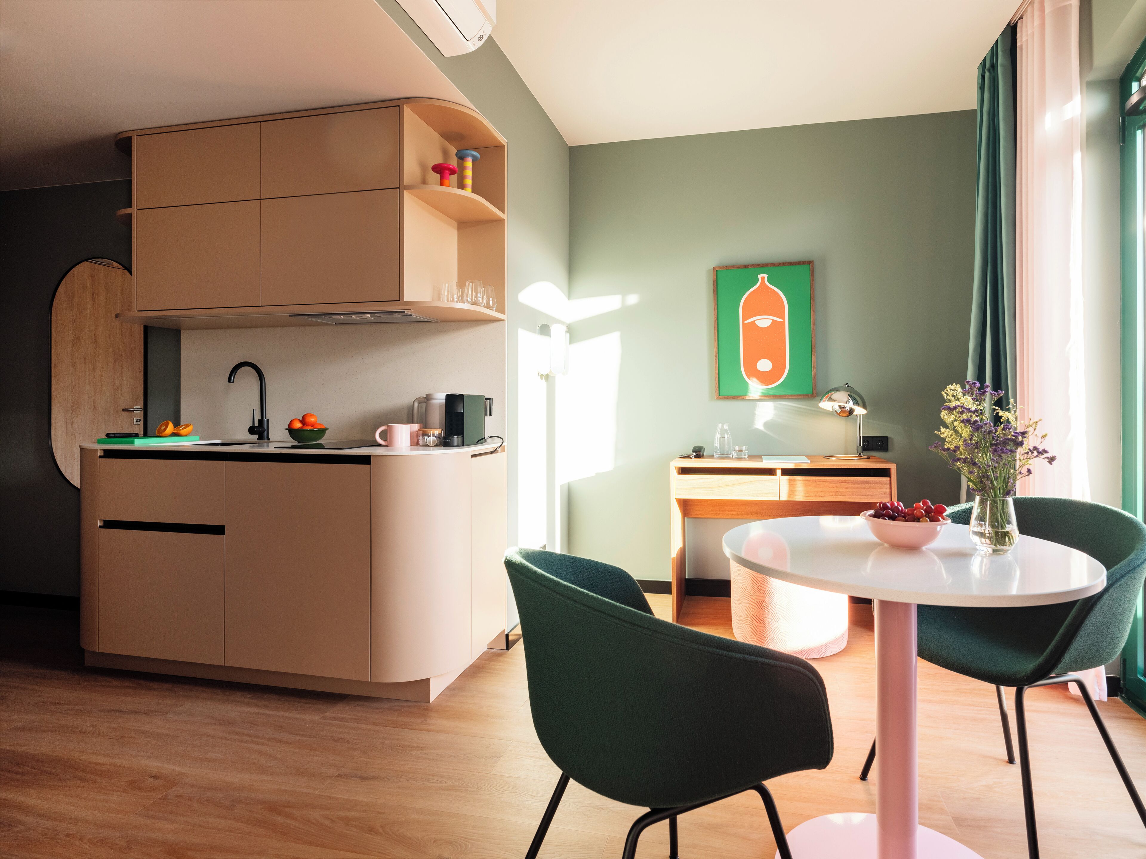A modern kitchen with a built-in oven, a coffee machine, and a sink. There is a dining area with a round table and two chairs.