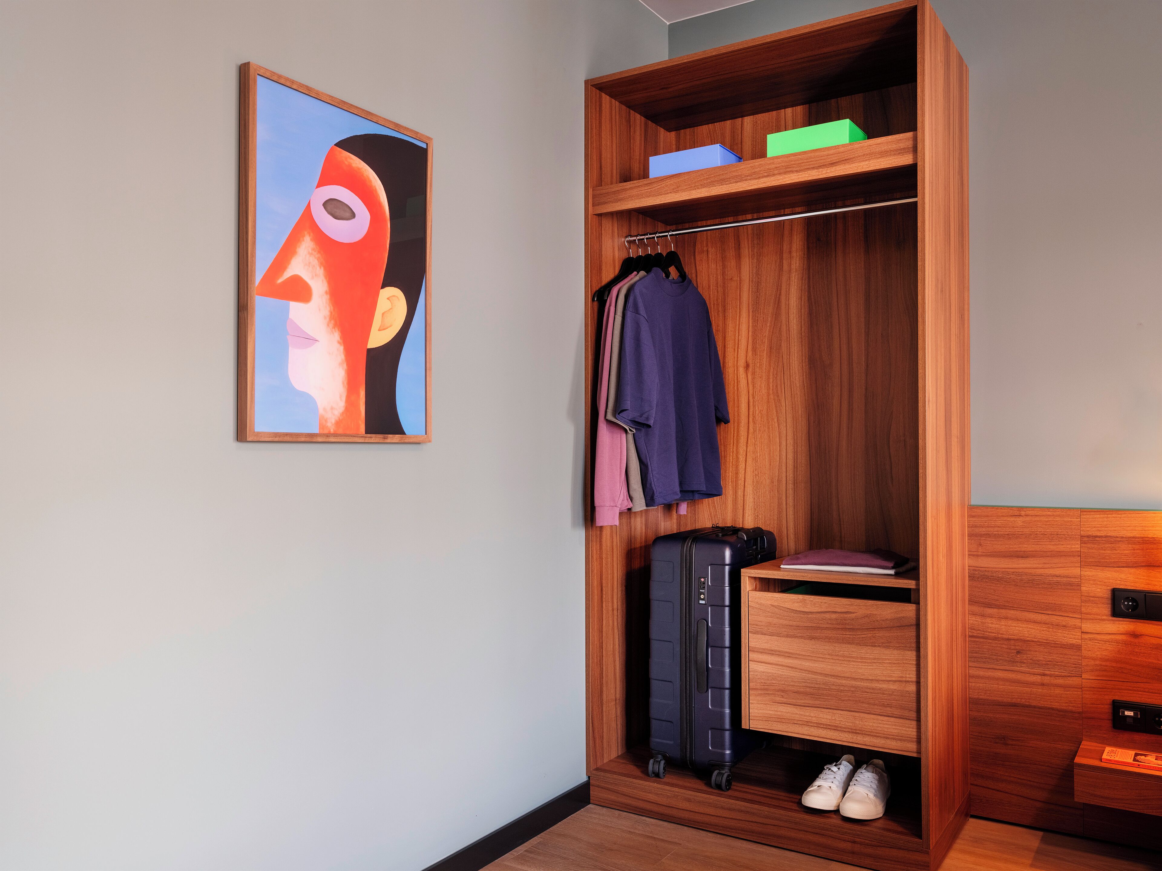 Ein Holzschrank mit Kleidung, einem Koffer und Schuhen.