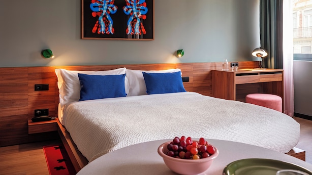 A hotel room with a bed, a desk, a chair, a bowl of fruit, and artwork on the wall. - Numa Lisbon Anjos (Lisbon)
