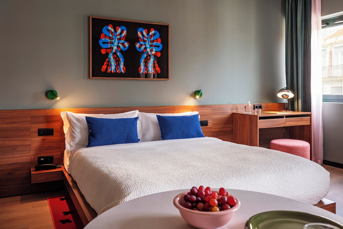 Een hotelkamer met een bed, een bureau, een stoel, een fruitschaal en kunst aan de muur.