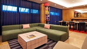A modern hotel room with a sectional sofa, a coffee table, and a dining area with a red carpet. - Numa Lisbon Anjos (Lisbon)