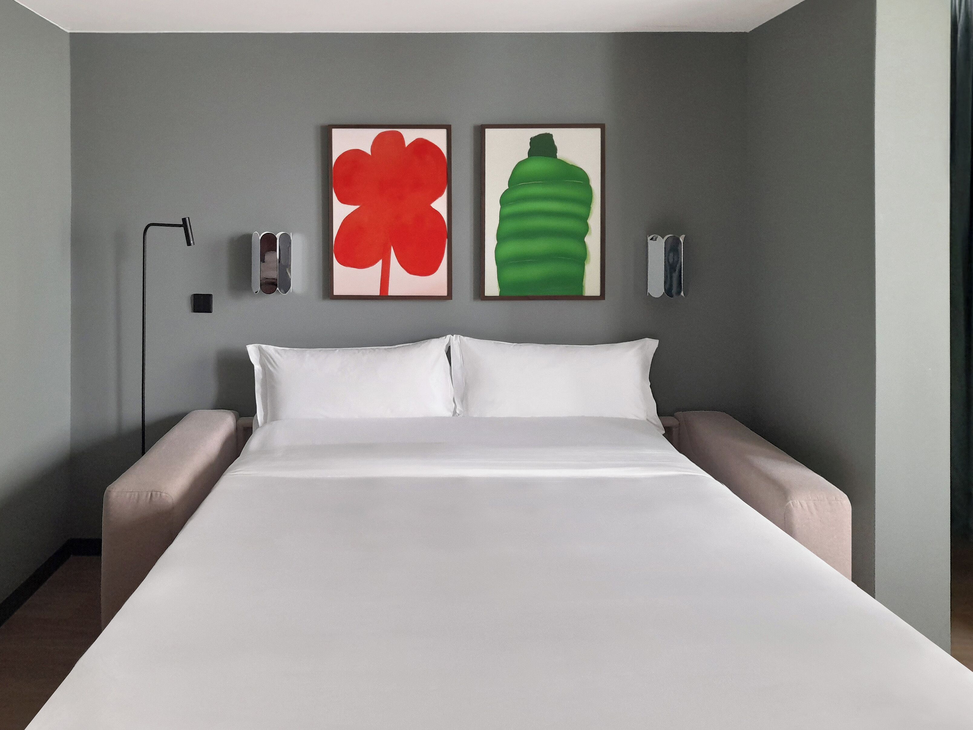 A hotel room with a large bed, two pillows, a nightstand, a lamp, and two wall-mounted speakers.