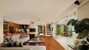 A modern living room with a sofa, coffee table, and a TV. There is a staircase leading to a balcony with plants.