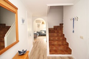 A staircase with wooden steps leading to a second floor, a wooden bench with a decorative bowl, and a coat rack with a blue item hanging.
