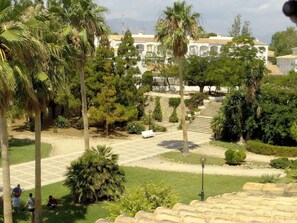 A courtyard with palm trees, a white building with arches, and a staircase leading to an upper level.