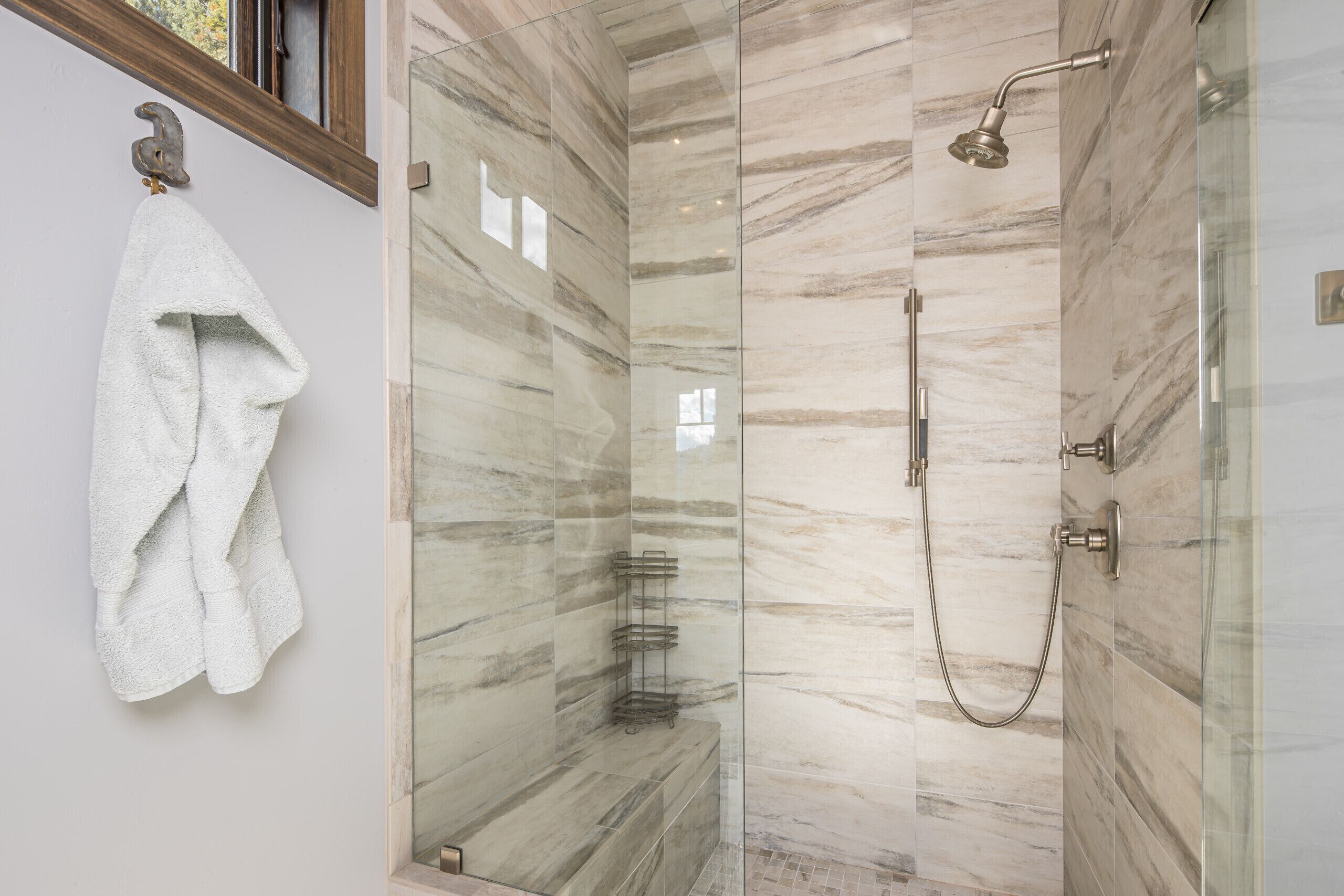 A modern bathroom with a glass-enclosed shower, marble walls, and a towel hanging on a hook.