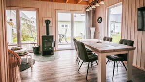 A cozy room with a wooden table and chairs, a fireplace, and large windows. - Schwalbennest - Infrared Sauna, Fireplace, 4 Sun Loungers, EV Charging Station (Olpenitz)