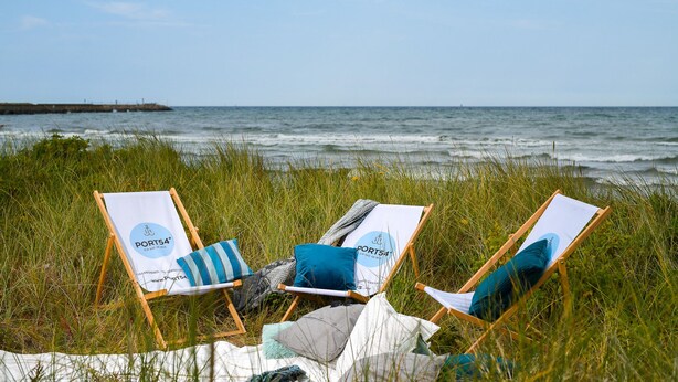 Two beach chairs with a blanket and pillows on a grassy area by the sea. - Schwalbennest - Infrared Sauna, Fireplace, 4 Sun Loungers, EV Charging Station (Olpenitz)