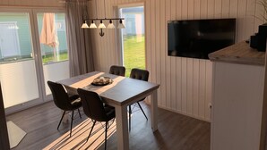 A dining area with a table, chairs, a chandelier, and a TV mounted on the wall. - Schwalbennest - Infrared Sauna, Fireplace, 4 Sun Loungers, EV Charging Station (Olpenitz)