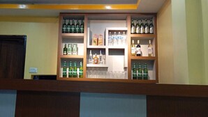 Uma área de bar com prateleiras cheias de bebidas engarrafadas e copos.