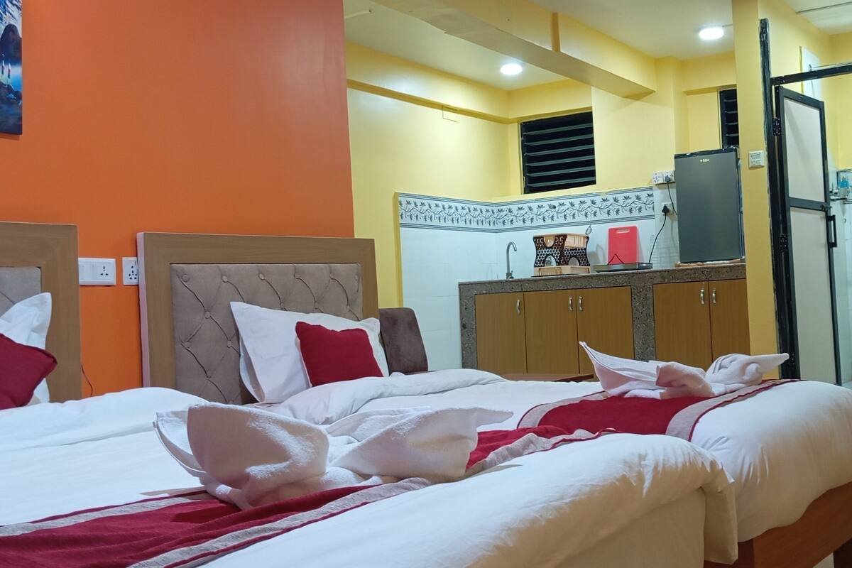 A hotel room with two beds, a kitchenette, and a shower area.