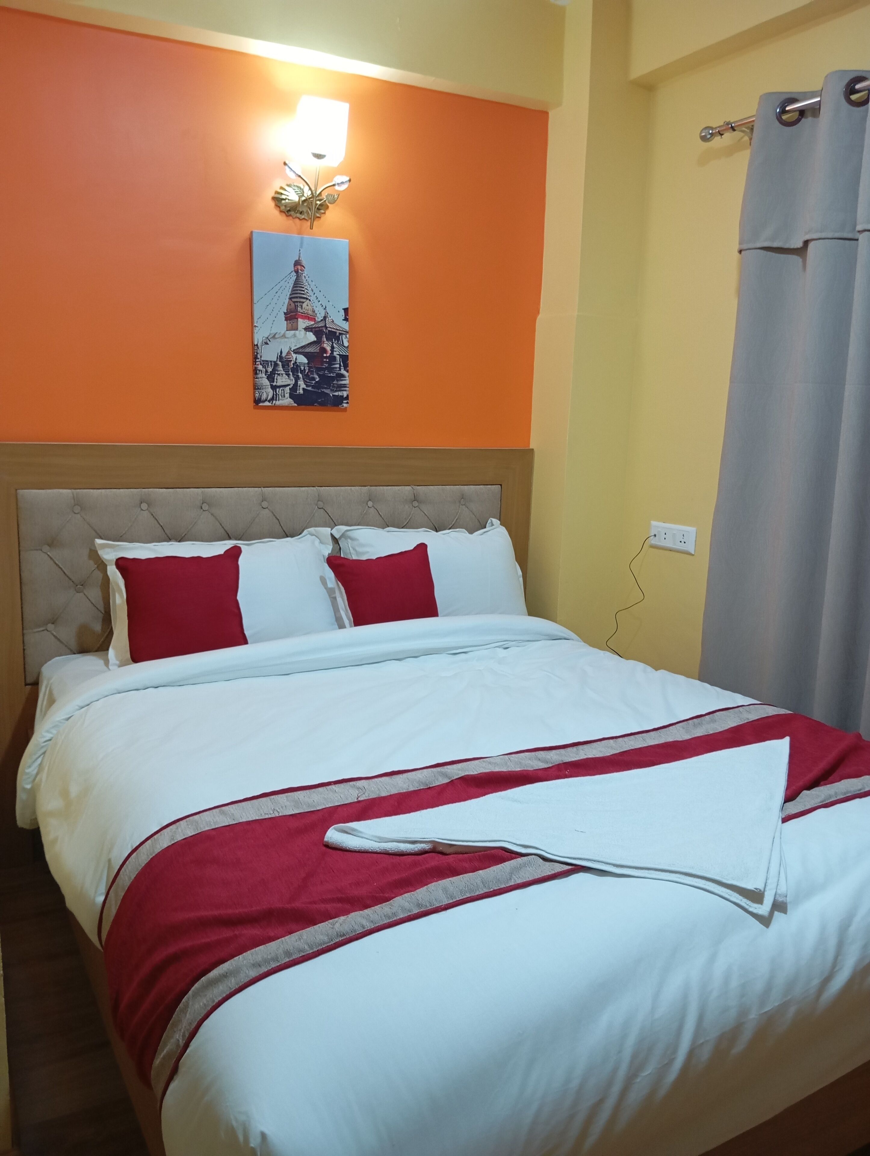 Una habitación de hotel con una cama, una lámpara fijada a la pared y un cuadro de un templo.