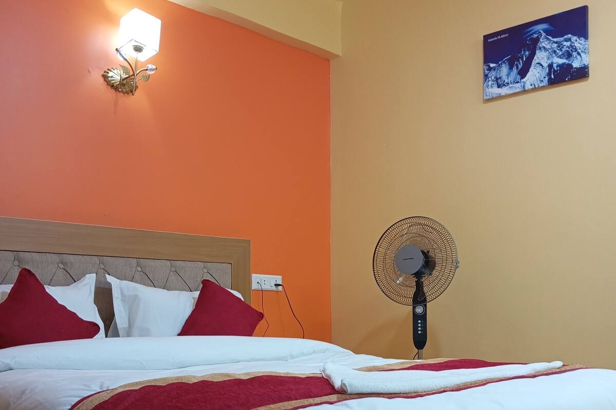 A neatly made bed with white and red bedding, a wooden headboard, a wall-mounted fan, and a framed picture on the wall.
