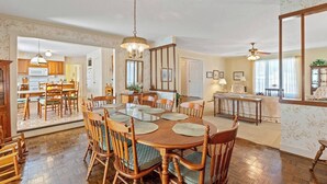 A spacious dining area with a large wooden table and chairs, a chandelier, and a view into the kitchen.